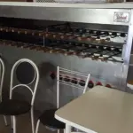 UMA CHURRASQUEIRA ROTATIVA A GÁS TOMASINI, 16 QUEIMADORES, 35 ESPETOS. COM OS ESPETOS.